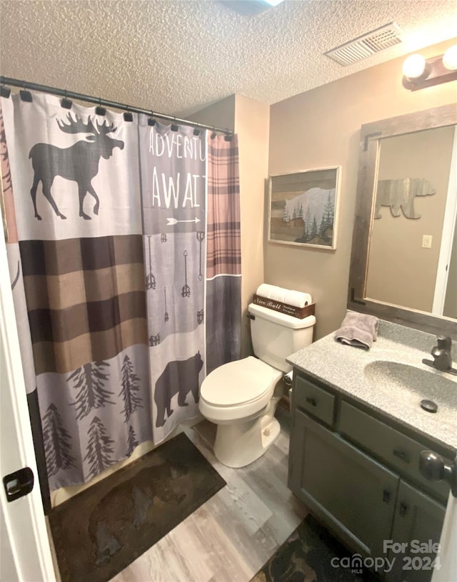 bathroom with walk in shower, hardwood / wood-style floors, a textured ceiling, toilet, and vanity