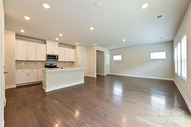 kitchen with white cabinets, dark wood-type flooring, stainless steel appliances, an island with sink, and decorative backsplash