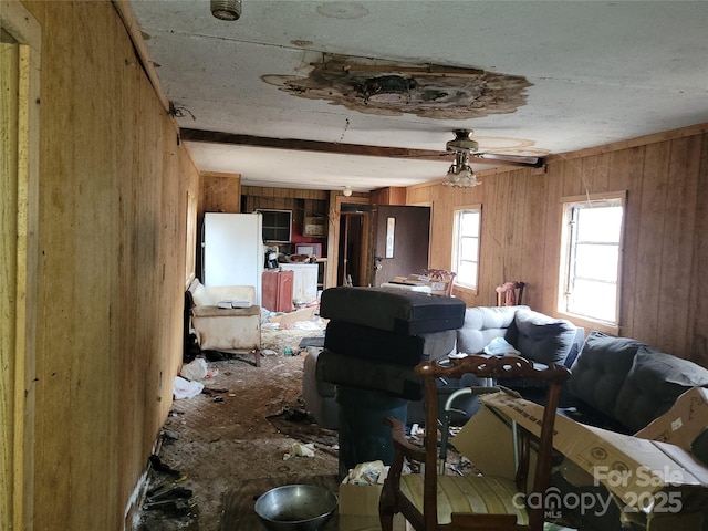 unfurnished living room with wooden walls, a ceiling fan, and beamed ceiling