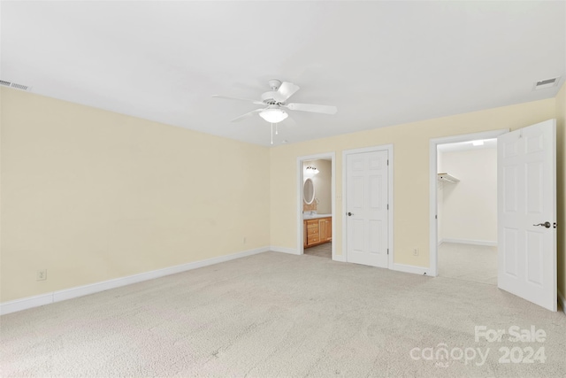 unfurnished bedroom featuring a walk in closet, ceiling fan, light colored carpet, and ensuite bathroom