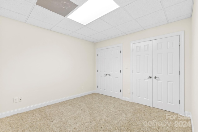 unfurnished bedroom featuring carpet flooring, a paneled ceiling, and multiple closets