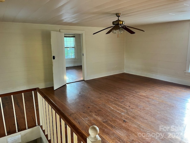 spare room featuring ceiling fan, wood walls, and dark hardwood / wood-style flooring