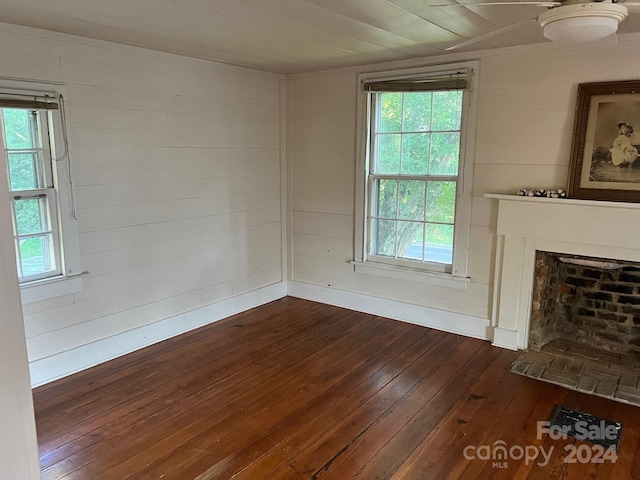 unfurnished living room with wood walls, dark wood-type flooring, and a wealth of natural light