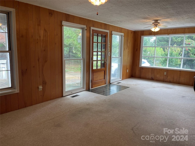 doorway to outside featuring carpet floors, wooden walls, and a textured ceiling