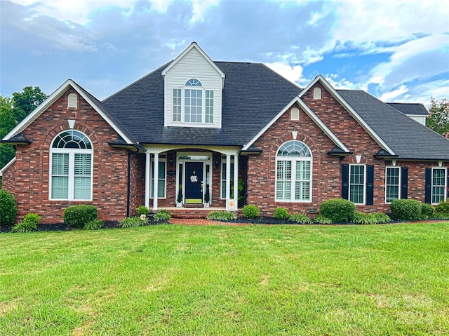 view of front of house with roof with shingles, brick siding, and a front lawn