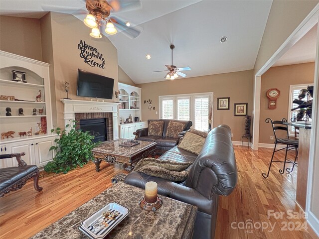 living room with light hardwood / wood-style floors, ceiling fan, a brick fireplace, lofted ceiling, and built in features