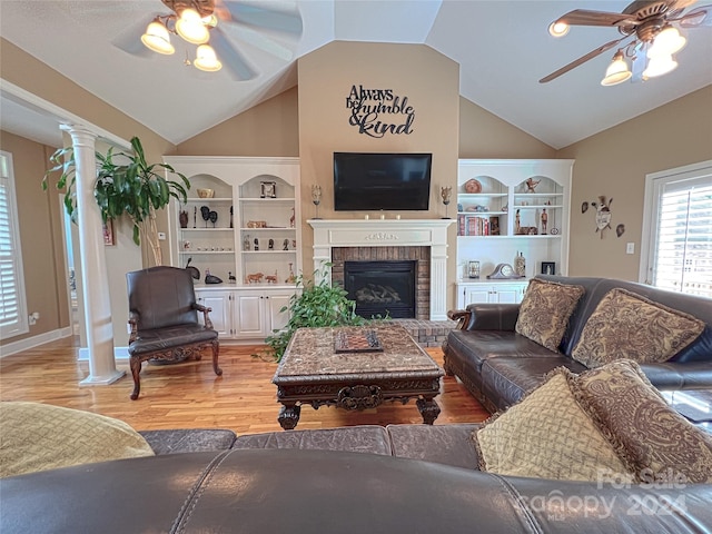 living room with ceiling fan, lofted ceiling, a brick fireplace, light hardwood / wood-style floors, and ornate columns