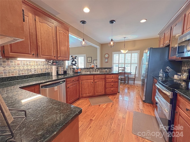 kitchen featuring stainless steel appliances, decorative backsplash, light wood-style floors, a sink, and a peninsula