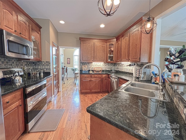 kitchen featuring a sink, appliances with stainless steel finishes, light wood finished floors, glass insert cabinets, and tasteful backsplash