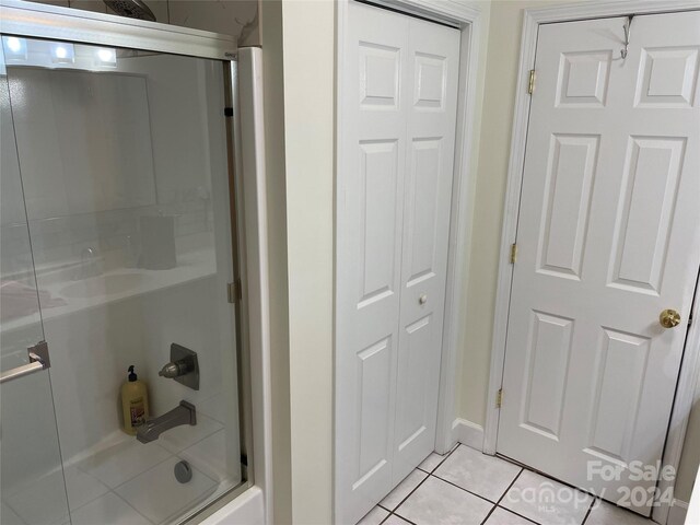 bathroom with bath / shower combo with glass door and tile patterned floors