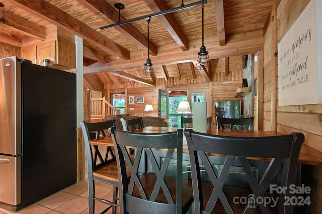 kitchen featuring wooden ceiling, wooden walls, light tile patterned floors, beamed ceiling, and stainless steel refrigerator