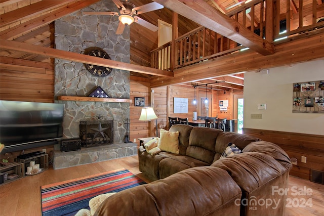 living room with beam ceiling, ceiling fan, a stone fireplace, wood walls, and hardwood / wood-style flooring