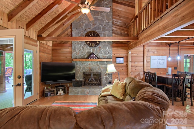 living room featuring wood walls, high vaulted ceiling, a stone fireplace, ceiling fan, and beamed ceiling