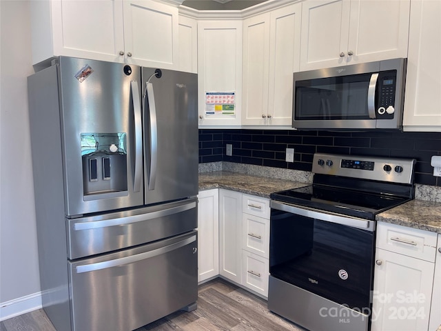 kitchen with wood-type flooring, dark stone counters, decorative backsplash, white cabinets, and stainless steel appliances