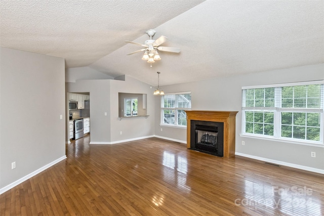 unfurnished living room with a textured ceiling, ceiling fan with notable chandelier, dark wood-type flooring, and vaulted ceiling