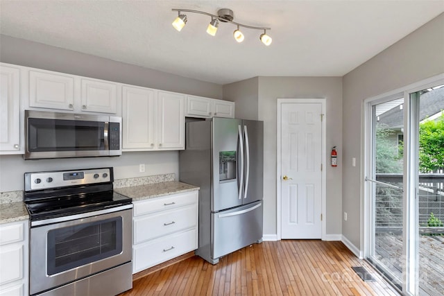 kitchen with light stone countertops, appliances with stainless steel finishes, light hardwood / wood-style floors, and white cabinetry