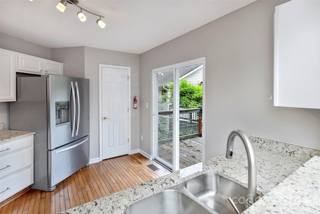 kitchen with light stone countertops, sink, white cabinetry, and stainless steel refrigerator with ice dispenser