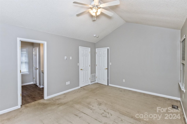 unfurnished bedroom with a textured ceiling, ceiling fan, light colored carpet, and vaulted ceiling