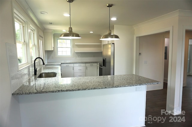 kitchen featuring kitchen peninsula, white cabinets, hanging light fixtures, light stone counters, and sink