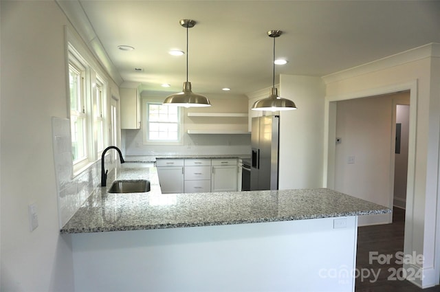 kitchen with kitchen peninsula, hanging light fixtures, light stone countertops, white cabinets, and sink