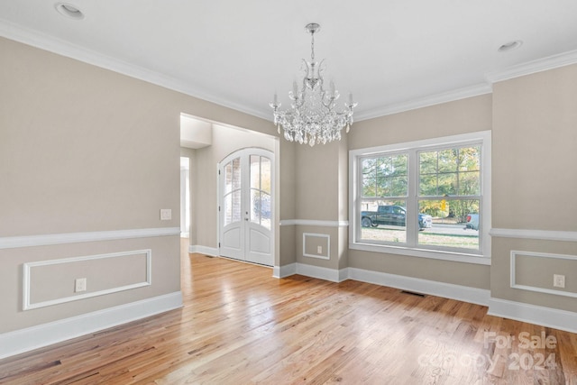 unfurnished dining area featuring a chandelier, light wood-style flooring, baseboards, french doors, and ornamental molding