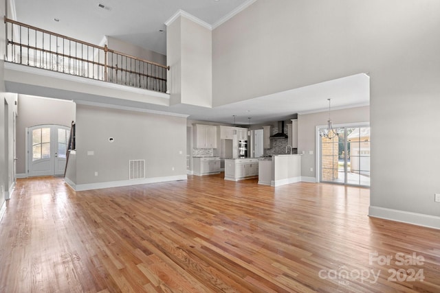 unfurnished living room with a high ceiling, ornamental molding, a chandelier, light wood finished floors, and baseboards