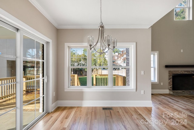 unfurnished dining area with crown molding, a fireplace, an inviting chandelier, and light wood-type flooring