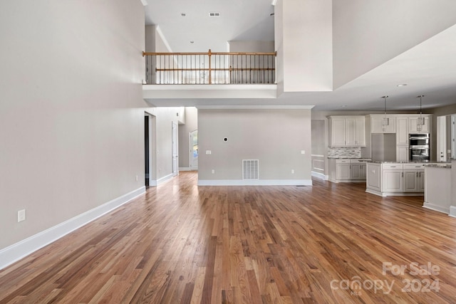 unfurnished living room with light wood-style floors, baseboards, and a high ceiling