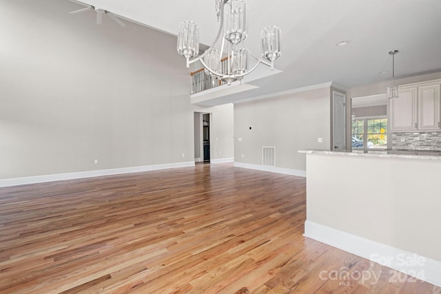 unfurnished living room featuring an inviting chandelier, light hardwood / wood-style flooring, and crown molding