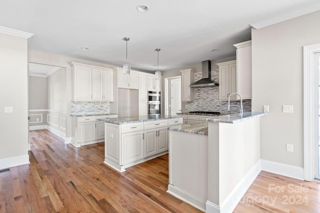 kitchen featuring light wood-type flooring, wall chimney range hood, pendant lighting, white cabinets, and a center island