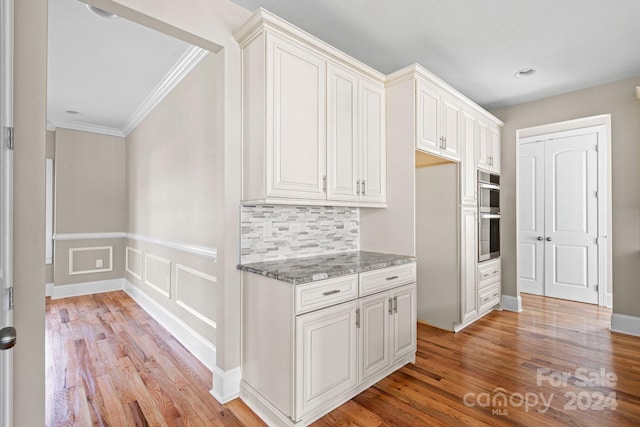 kitchen featuring stone countertops, light wood-style flooring, crown molding, white cabinets, and tasteful backsplash