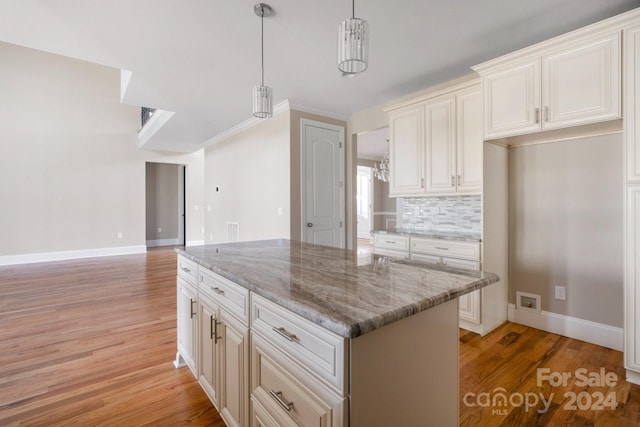 kitchen featuring light wood-style flooring, light stone countertops, decorative light fixtures, and a center island