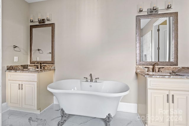 bathroom featuring marble look tiles, baseboards, two vanities, and a soaking tub