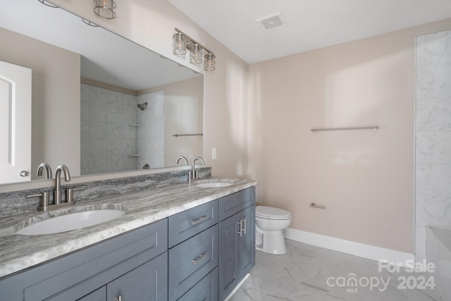 full bath with marble look tile flooring, tiled shower, double vanity, toilet, and baseboards