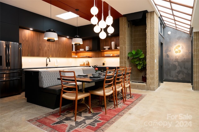 kitchen with sink, a breakfast bar area, stainless steel fridge, pendant lighting, and wall chimney range hood