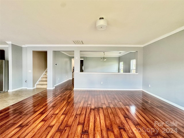 unfurnished living room featuring hardwood / wood-style flooring, an inviting chandelier, and crown molding