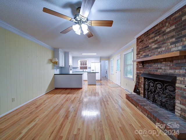 unfurnished living room with light wood-type flooring, a brick fireplace, ornamental molding, a textured ceiling, and wood walls