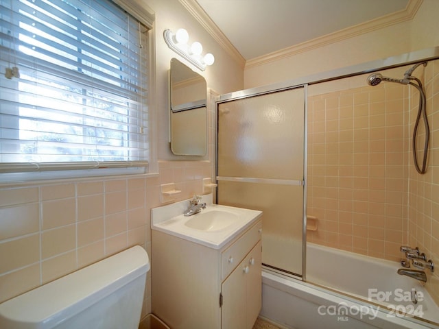 full bathroom featuring crown molding, toilet, shower / bath combination with glass door, vanity, and tile walls