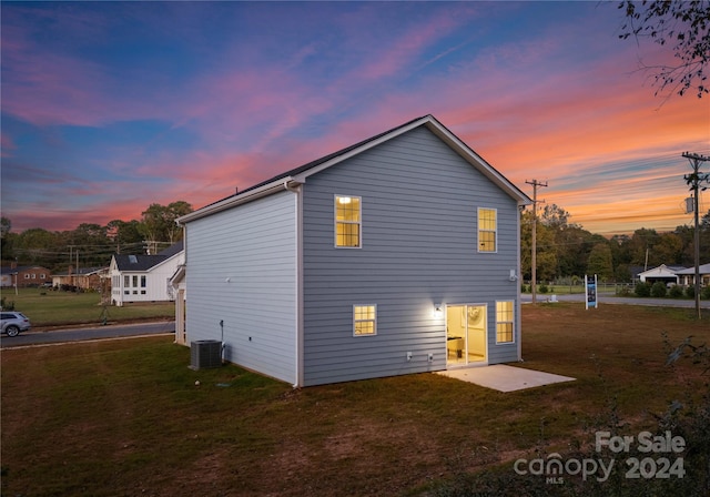 back house at dusk featuring a patio area, cooling unit, and a yard