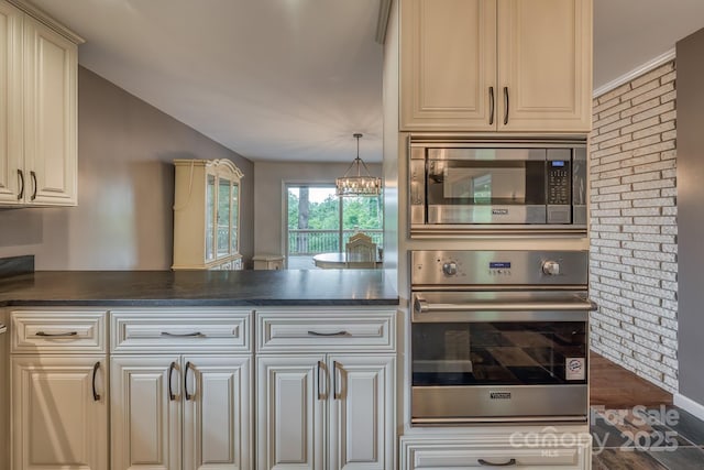 kitchen featuring appliances with stainless steel finishes, hanging light fixtures, kitchen peninsula, cream cabinets, and an inviting chandelier