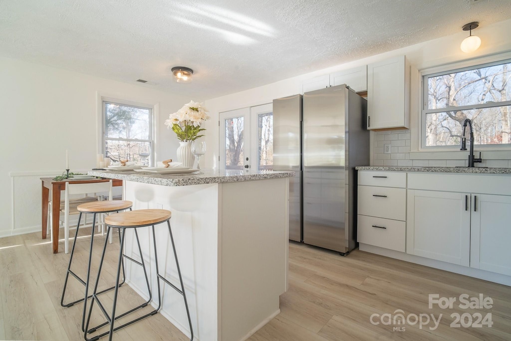 kitchen with white cabinetry, a kitchen island, a healthy amount of sunlight, and light wood-type flooring