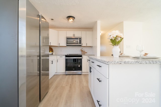 kitchen featuring white cabinetry, tasteful backsplash, light hardwood / wood-style flooring, a textured ceiling, and appliances with stainless steel finishes