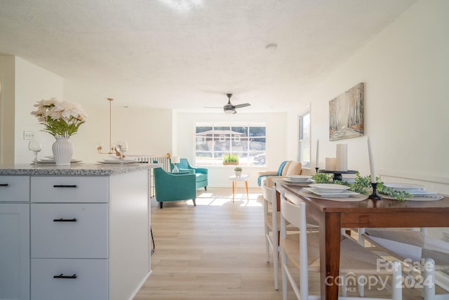 interior space featuring ceiling fan, white cabinetry, a textured ceiling, decorative light fixtures, and light wood-type flooring