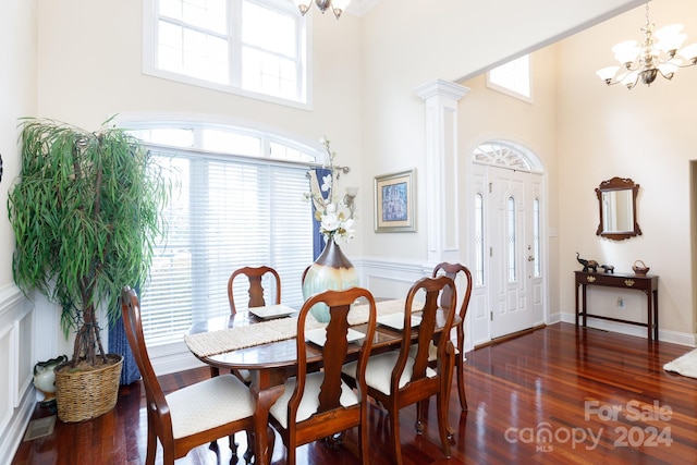 dining area featuring a towering ceiling, ornate columns, dark wood-type flooring, and a notable chandelier