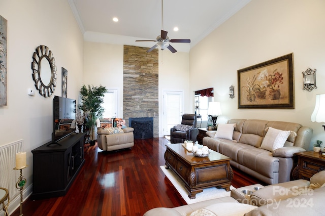 living room with a towering ceiling, dark hardwood / wood-style flooring, a stone fireplace, and ornamental molding