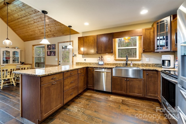 kitchen with light stone countertops, dark hardwood / wood-style flooring, kitchen peninsula, decorative light fixtures, and appliances with stainless steel finishes