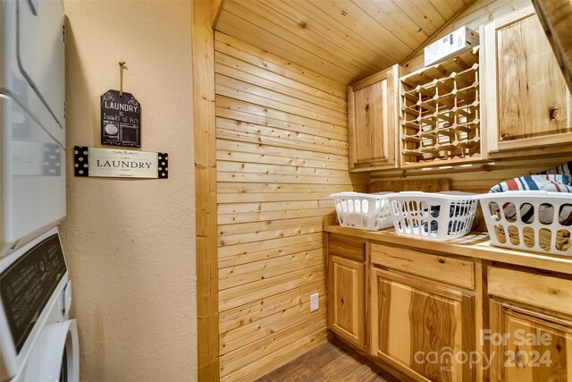 clothes washing area featuring cabinets, wooden ceiling, stacked washer / dryer, and wooden walls