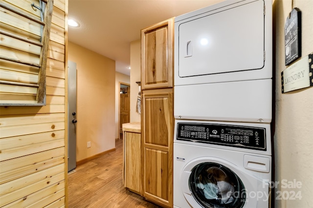 laundry room featuring stacked washer / dryer, cabinets, and light hardwood / wood-style floors