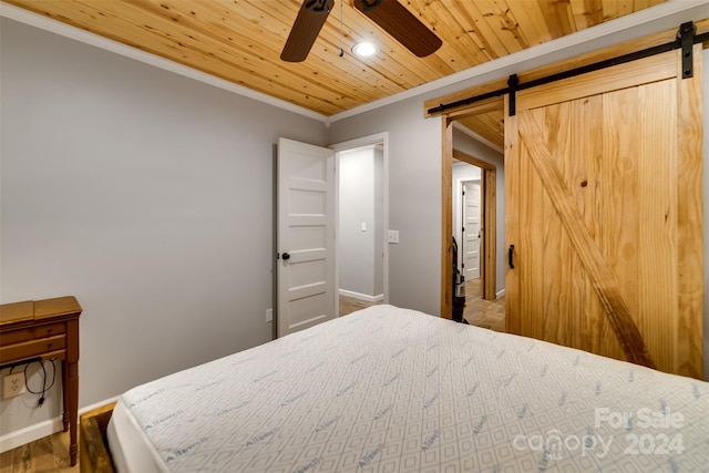 bedroom featuring ceiling fan, a barn door, wood-type flooring, wood ceiling, and ornamental molding