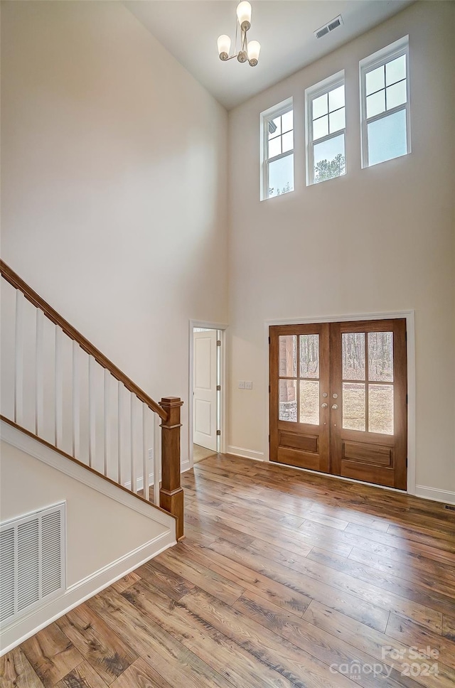 entrance foyer with light wood-type flooring, a towering ceiling, and french doors